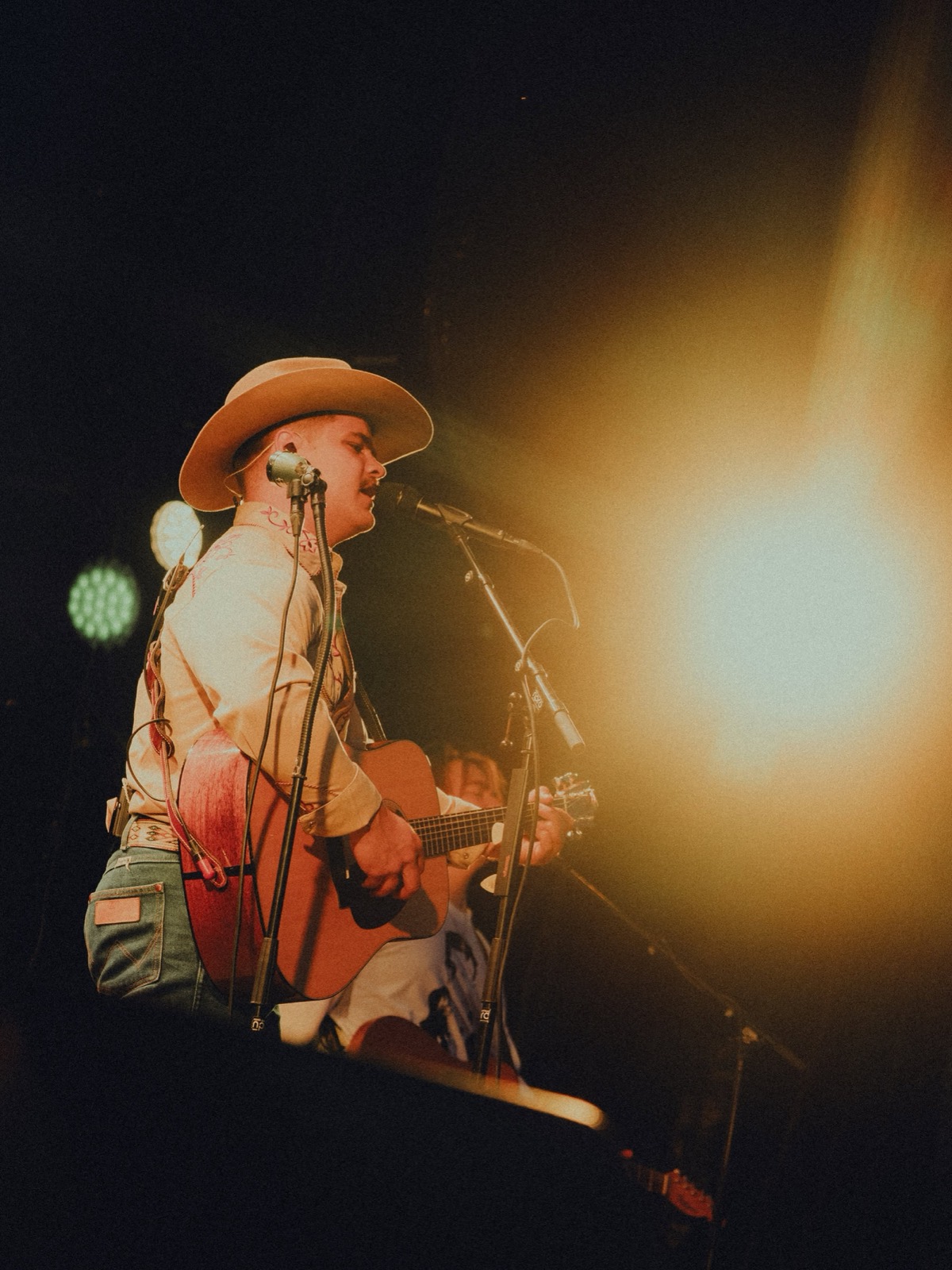 Artist med cowboyhatt og gitar i varmt motlys på scenen
